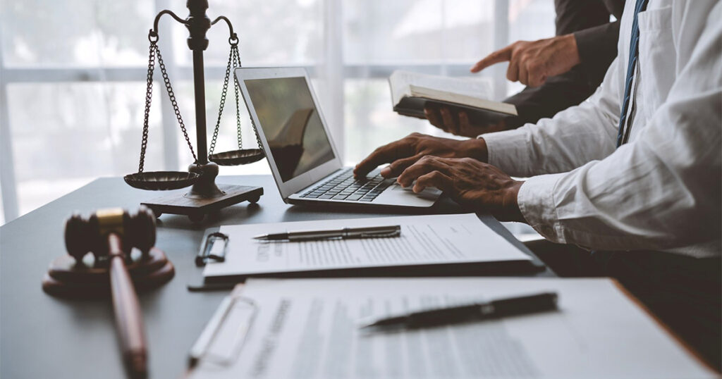 A man in a suit sits at a desk with a laptop and a scale, contemplating personal injury settlements in Texas.