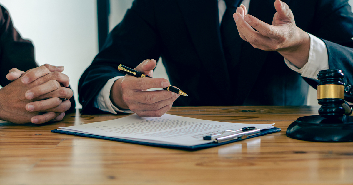 Two men in suits discussing personal injury settlements at a table with a pen and paper in Houston, Texas.