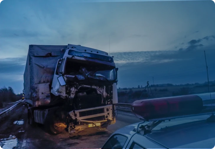 Damaged semi-truck on the side of a wet road at dusk after a collision, highlighting the need for a truck accident lawyer.