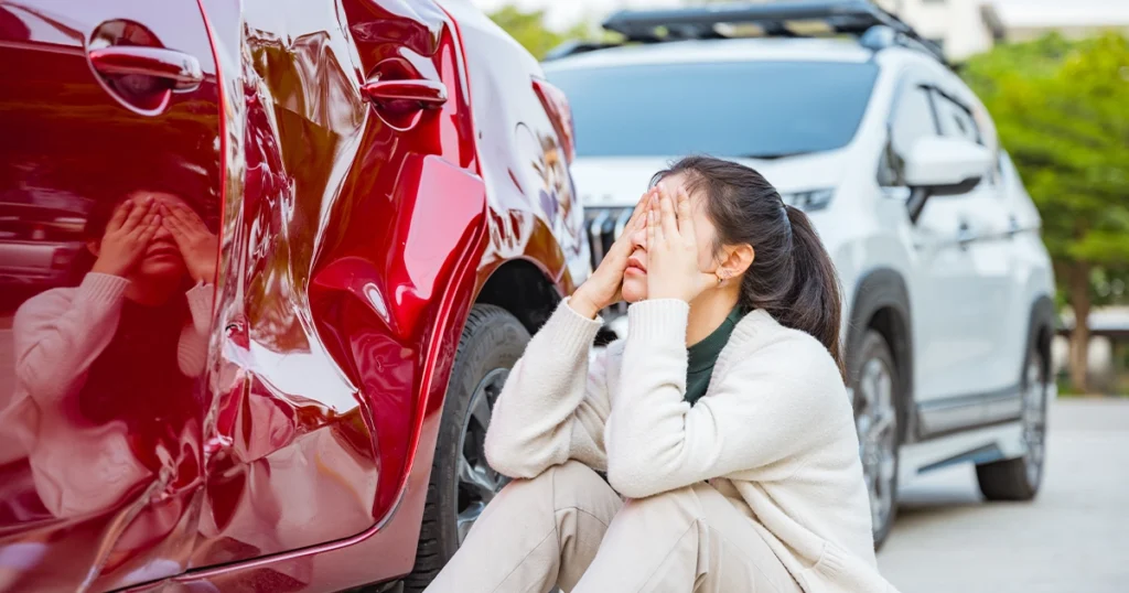 Woman distressed by car accident, sitting by damaged vehicle